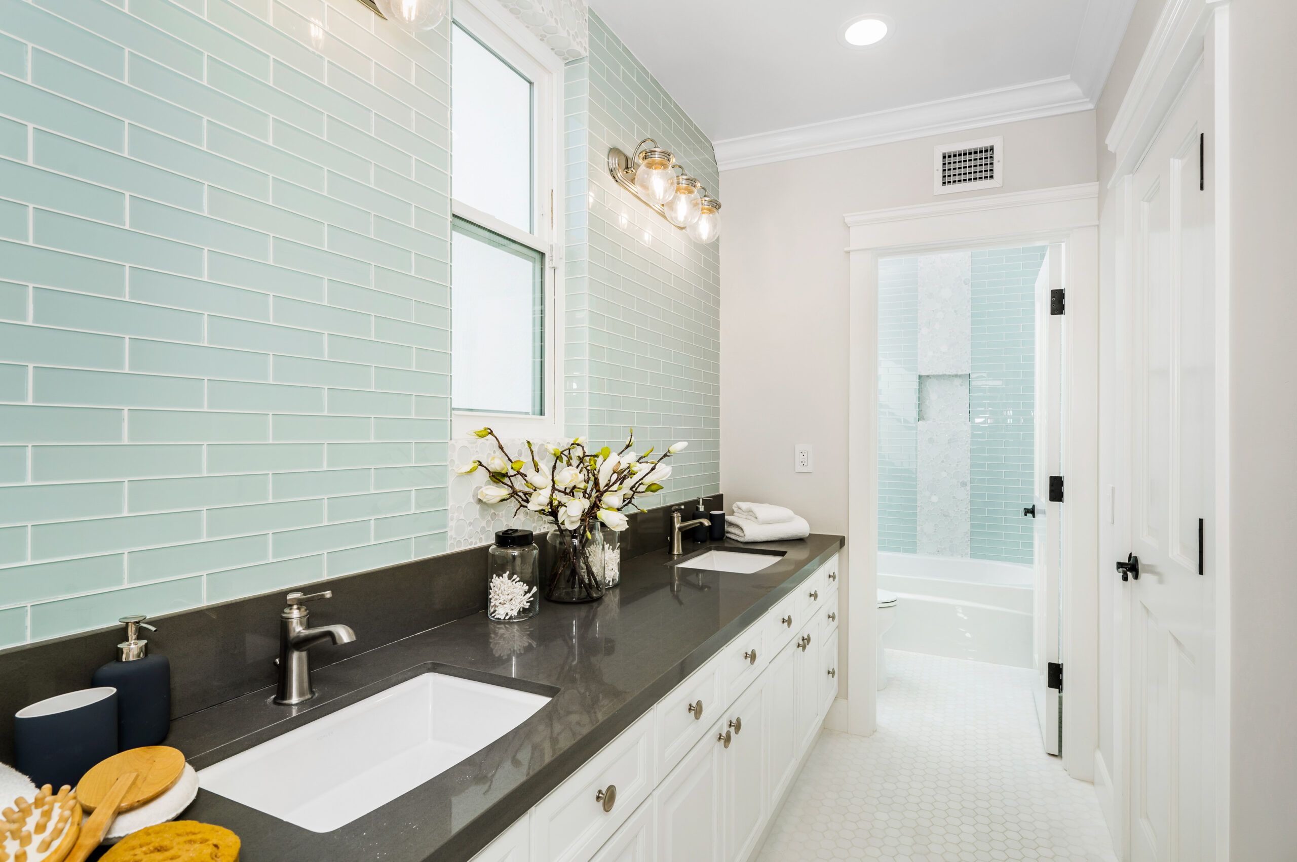 A spacious blue tiled bathroom with a glass shower and dual sinks